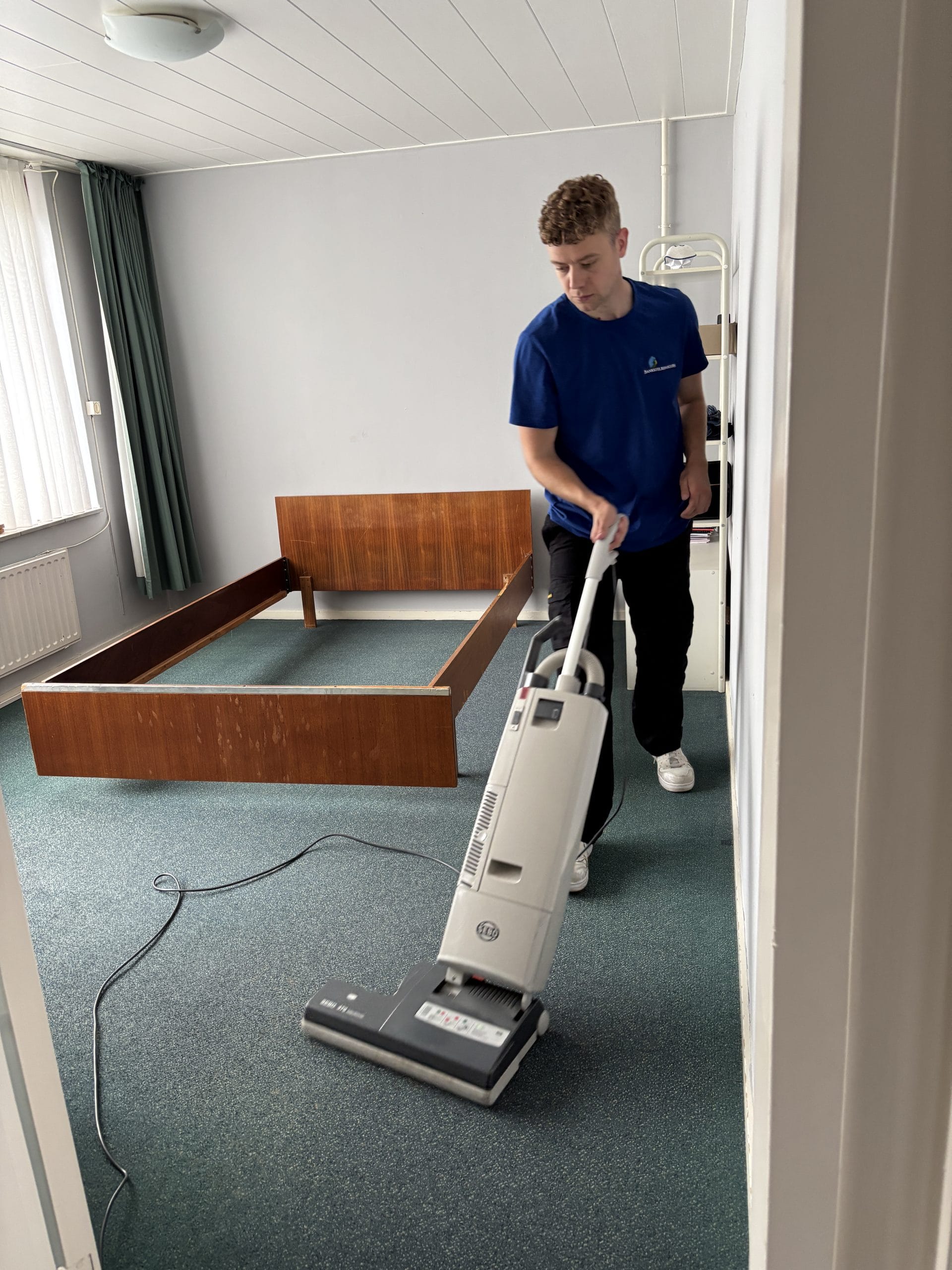 Dennis zuigt vloerbedekking in een leeggehaalde slaapkamer